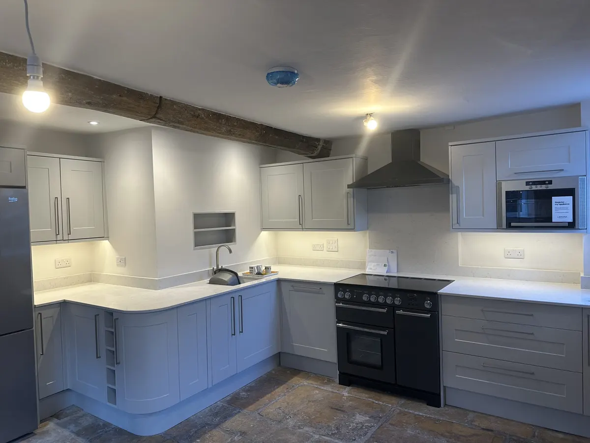 Cottage kitchen with oak beam, white cupboards, visible sockets and under-cabinet lighting