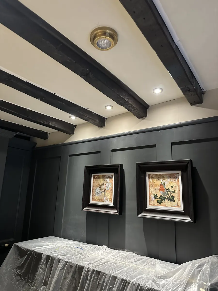 Dark panelled room with exposed beams, recessed ceiling lights and furniture covered for work