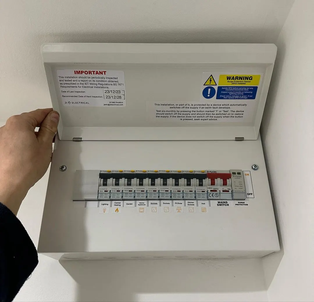 Hand opening the cover of a white consumer unit with warning labels and circuit breakers