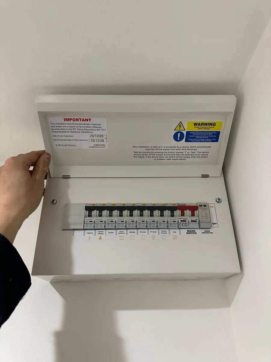 White consumer unit with its hinged lid raised, labelled circuit switches, red main switch and inspection label
