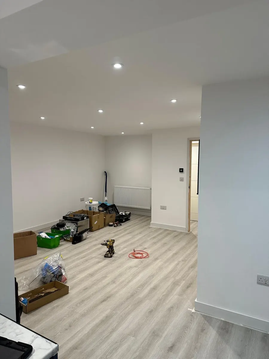Open room with illuminated ceiling downlights, wall sockets, radiator and tools and boxes on the floor
