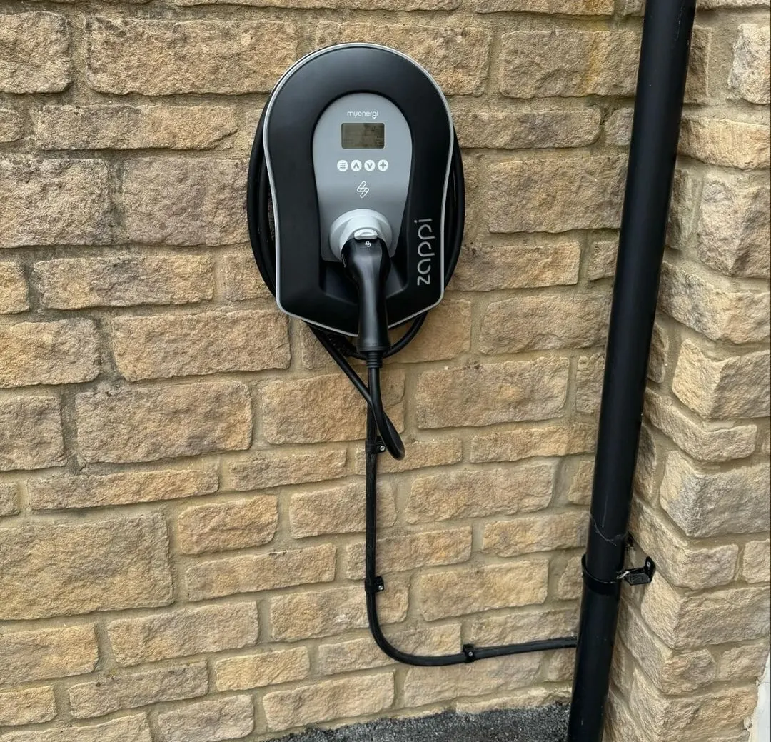 Black and grey zappi chargepoint on a stone wall with cable beside a black downpipe