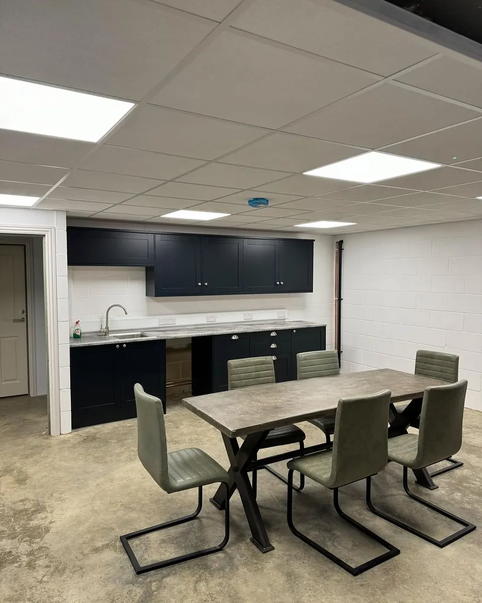 Staff kitchen with ceiling light panels, wall sockets, dark cabinets and a dining table