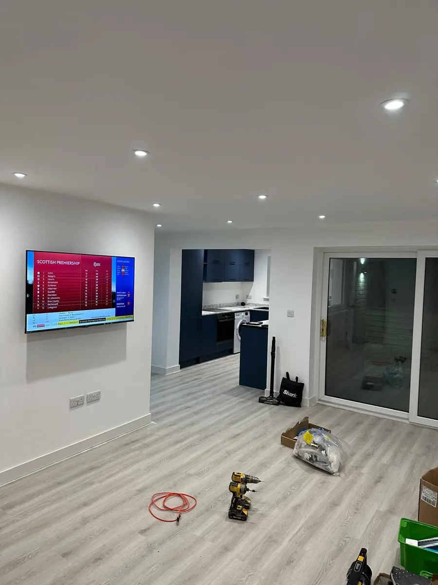 Living area with wall-mounted television, downlights, low wall sockets and patio doors beside an open kitchen