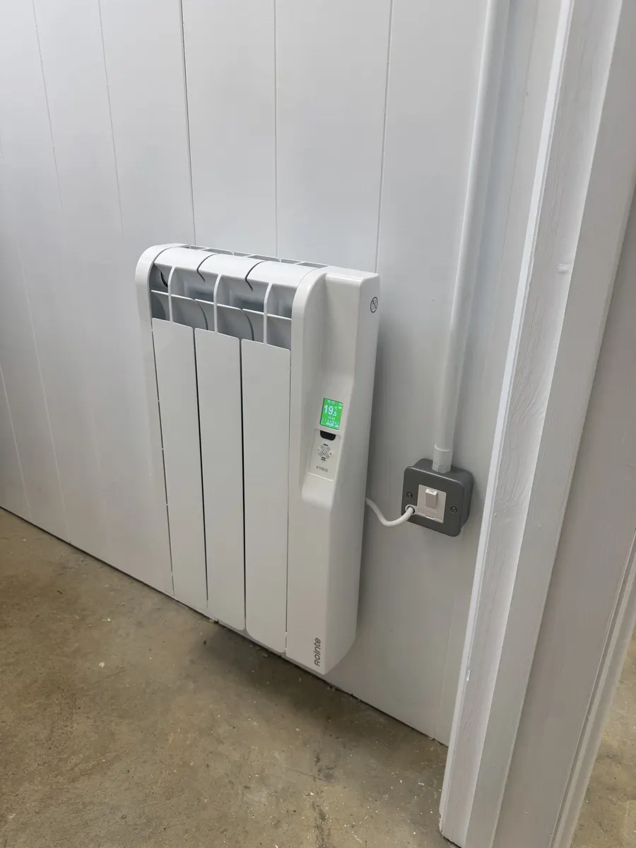 White electric radiator on a panelled wall with a short cable to a grey connection plate