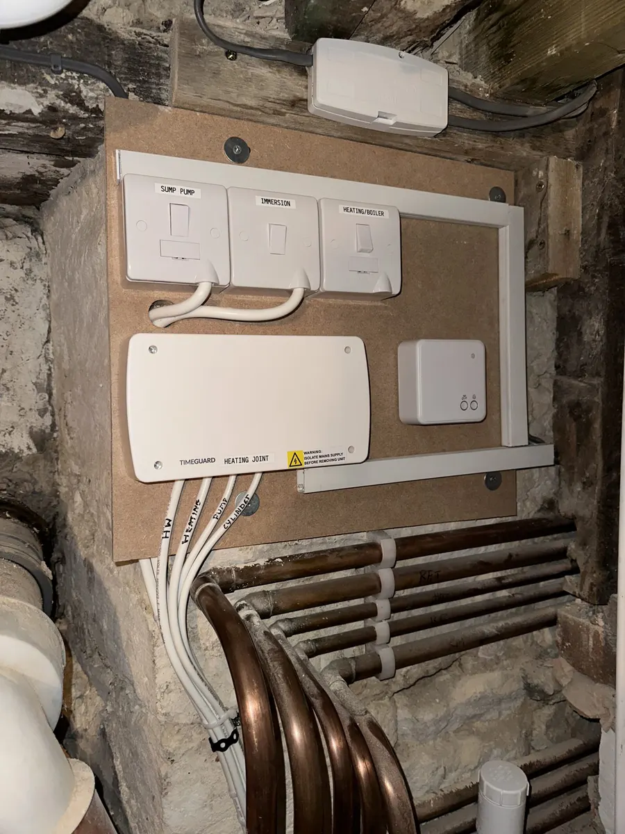 Labelled heating controls and fused switches mounted beside timber and stonework