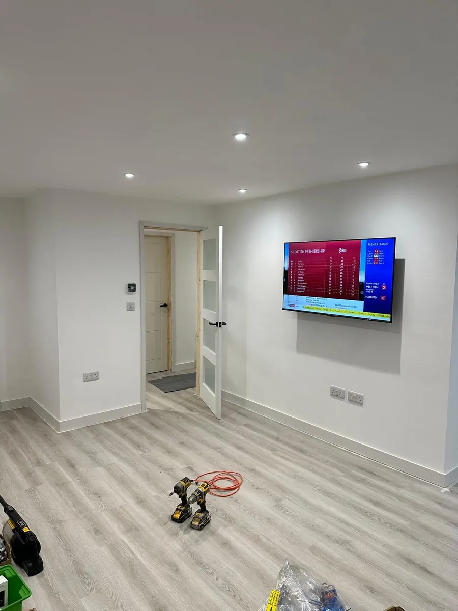 Open-plan living room with downlights, wall-mounted TV and double sockets, tools on the floor