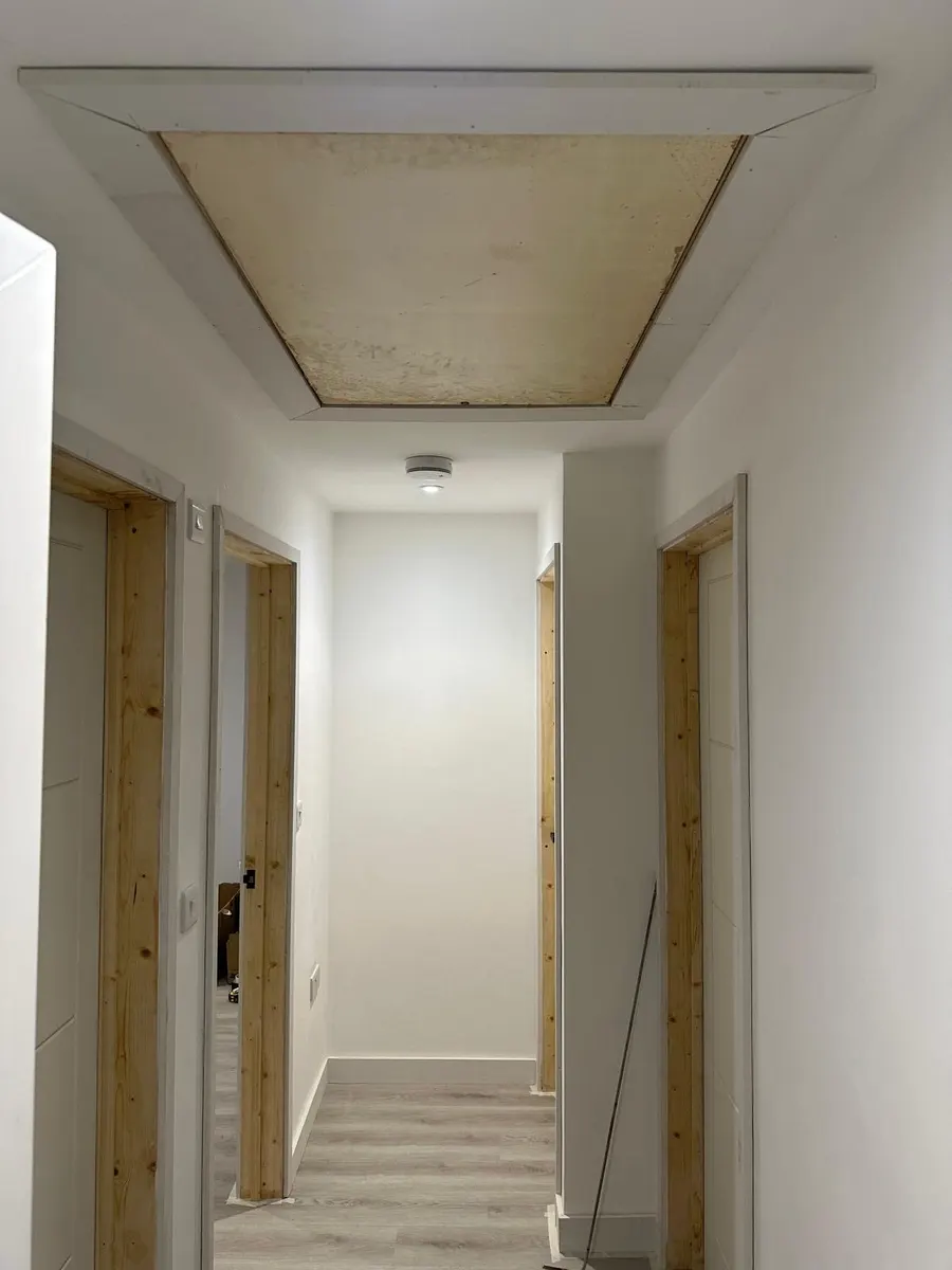 Finished hallway with a framed loft hatch, smoke alarm, switches and unpainted door linings