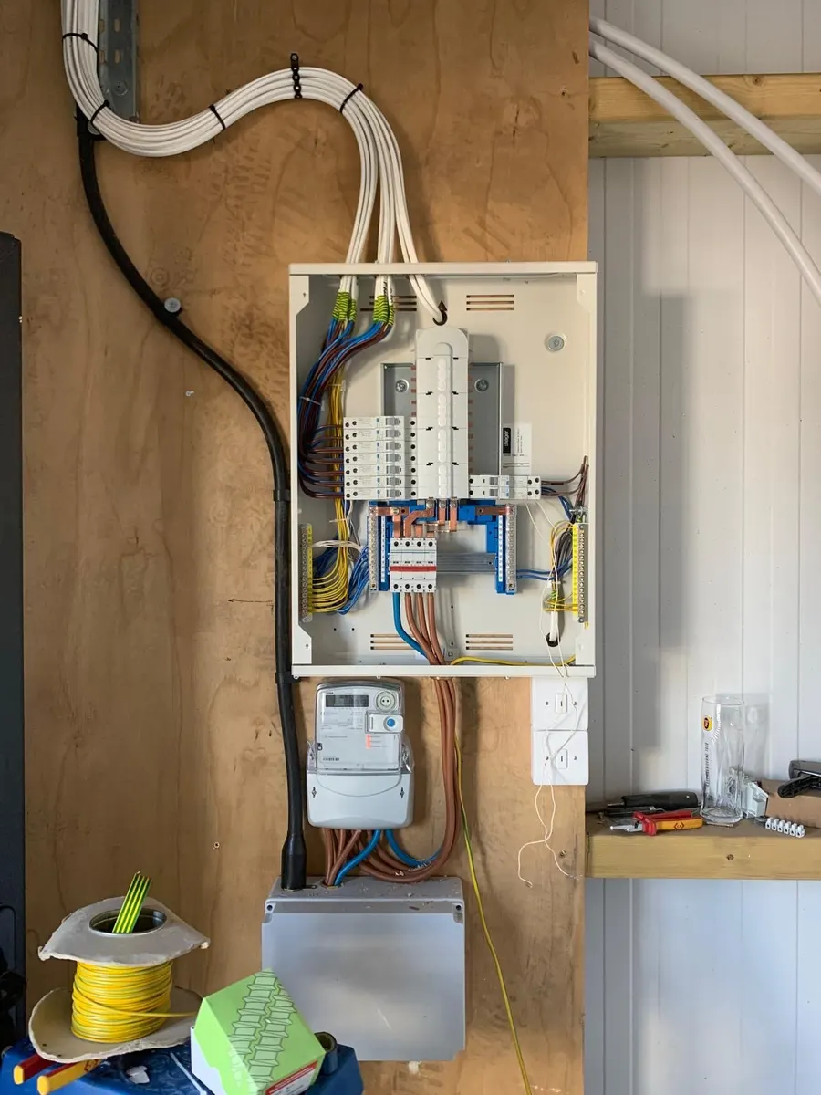 Distribution board and meter on a plywood backboard, cables bundled to the board, cable drum and tools below
