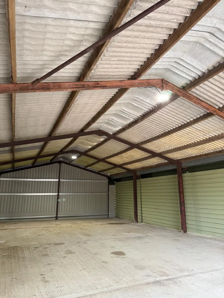 Steel portal-frame barn lit by LED high-bays, new wall cladding below a corrugated roof