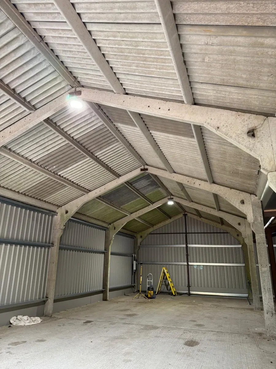 Concrete portal-frame barn with LED high-bays, new metal cladding, work light and stepladder on the floor