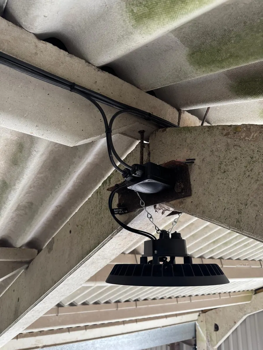 LED high-bay hung on a chain under a concrete beam, junction box and cable run above