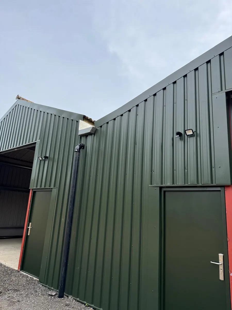 Corner of a green-clad barn with two personnel doors and external floodlights