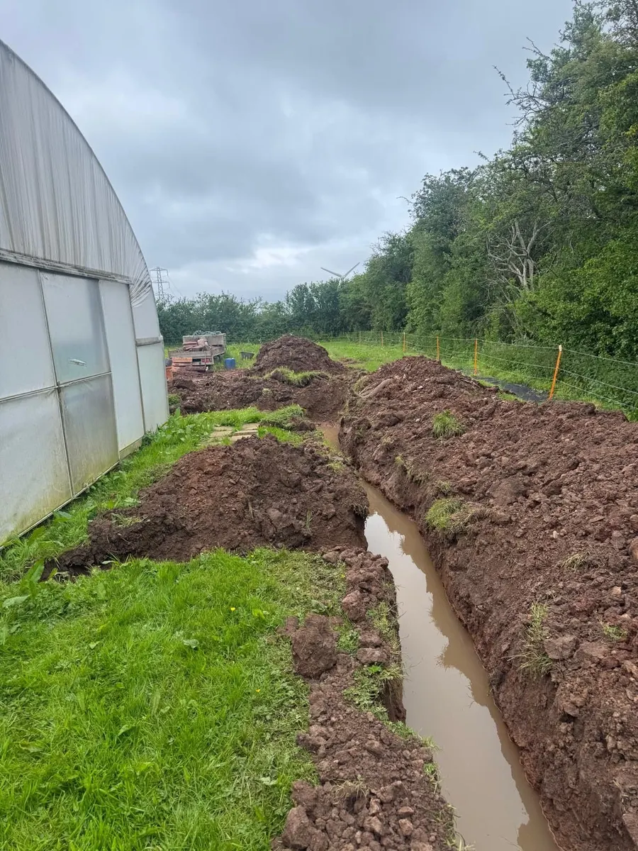 Trench beside a polytunnel with standing water and spoil heaps either side