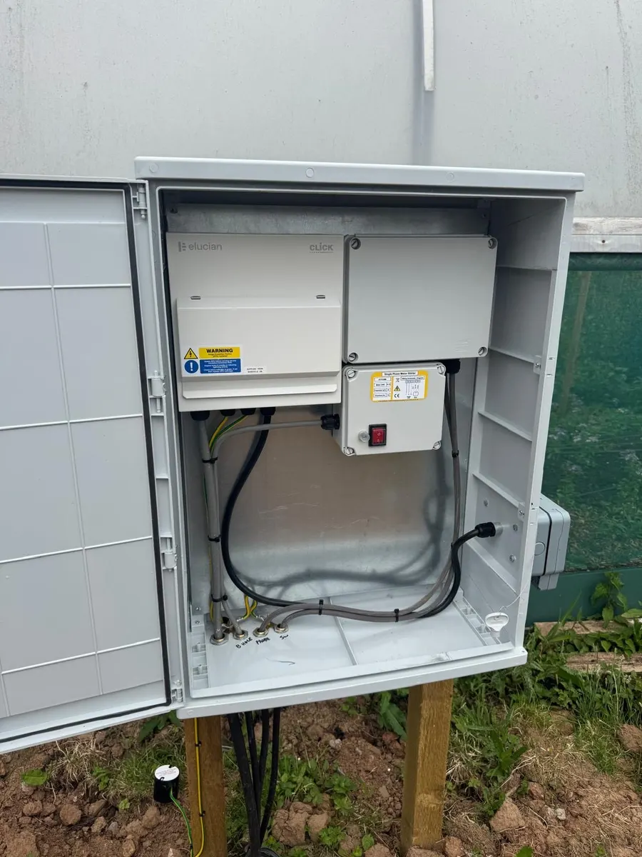 Enclosure open: consumer unit, junction box and single-phase pump starter with cable glands marked for the borehole and probe